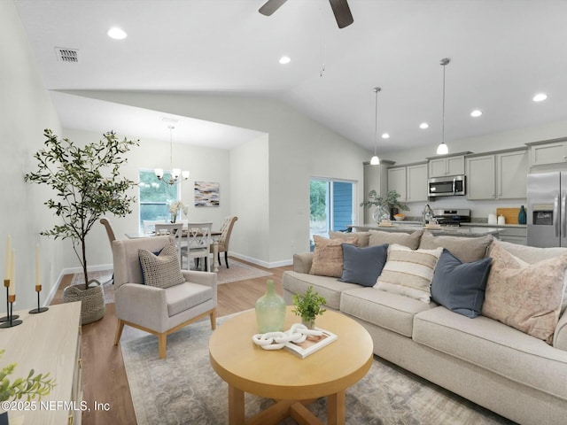 living room featuring vaulted ceiling, sink, ceiling fan with notable chandelier, and light hardwood / wood-style floors