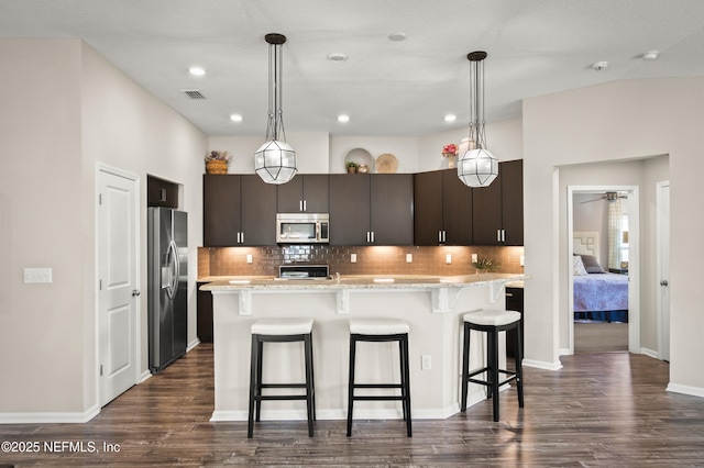 kitchen featuring hanging light fixtures, stainless steel appliances, dark brown cabinetry, light stone counters, and tasteful backsplash