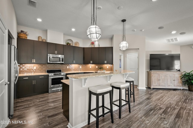 kitchen with appliances with stainless steel finishes, dark hardwood / wood-style floors, decorative light fixtures, decorative backsplash, and dark brown cabinets