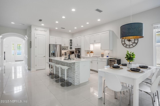 kitchen with a breakfast bar, white cabinetry, tasteful backsplash, an island with sink, and stainless steel appliances