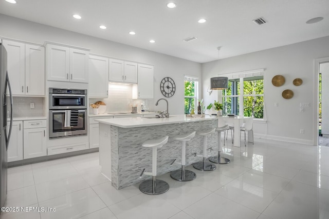 kitchen featuring white cabinetry, decorative backsplash, stainless steel appliances, and an island with sink