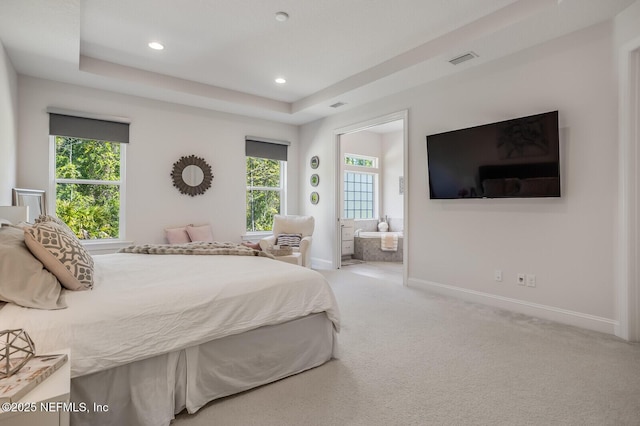 bedroom with a tray ceiling, ensuite bath, and light colored carpet