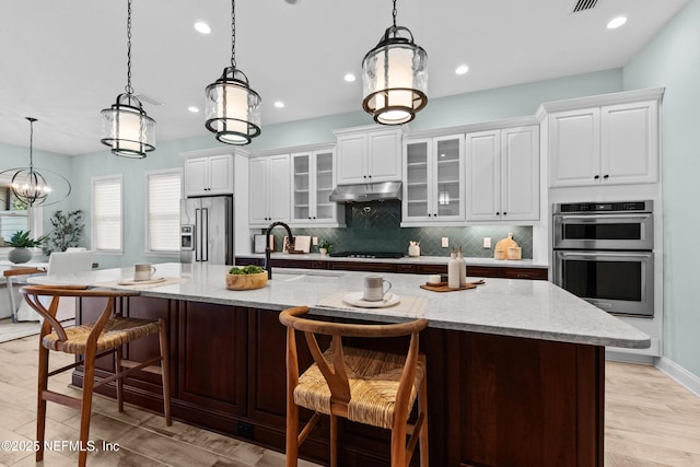 kitchen with pendant lighting, light stone countertops, a large island with sink, and appliances with stainless steel finishes