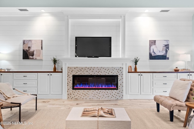 living room with a tiled fireplace, ornamental molding, and light wood-type flooring