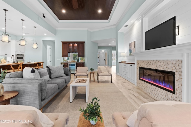 living room featuring sink, light wood-type flooring, ornamental molding, a raised ceiling, and a tile fireplace