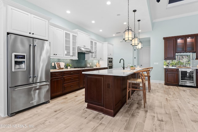 kitchen featuring a center island with sink, pendant lighting, stainless steel appliances, beverage cooler, and decorative backsplash