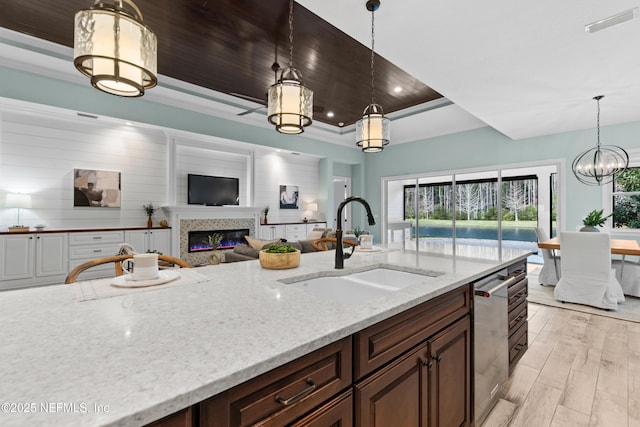 kitchen featuring decorative light fixtures, dishwasher, sink, a raised ceiling, and light stone countertops