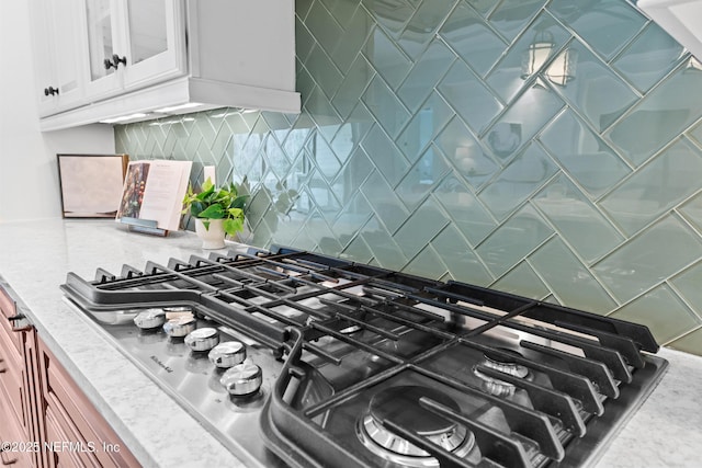 interior details with white cabinetry, stainless steel gas cooktop, and backsplash