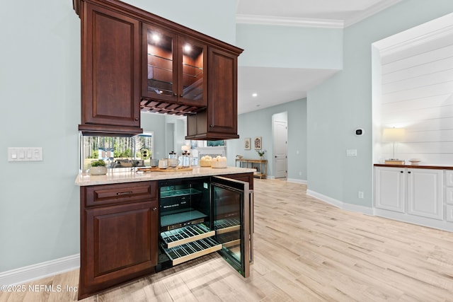 bar with dark brown cabinetry, light stone countertops, crown molding, and light hardwood / wood-style floors