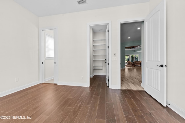 unfurnished bedroom featuring dark wood-type flooring, a walk in closet, and a closet