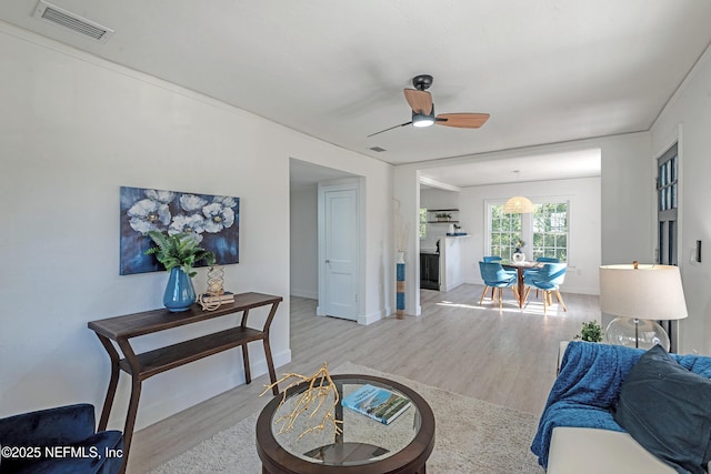 living room with light wood-type flooring, ceiling fan, and crown molding