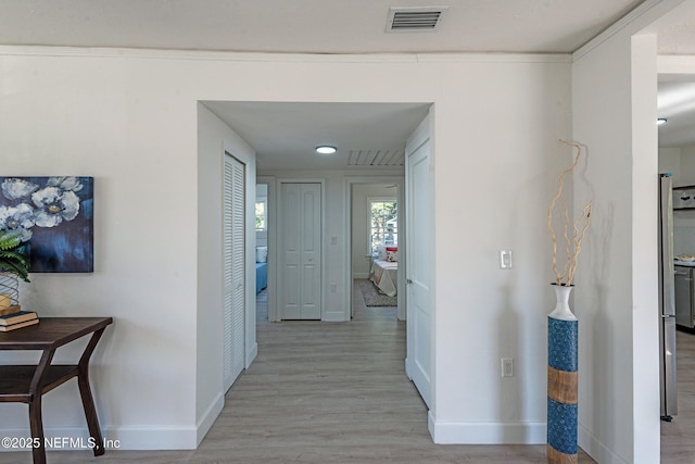 corridor with light wood-type flooring and ornamental molding