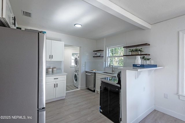 kitchen featuring stainless steel appliances, sink, white cabinets, stacked washer / dryer, and a kitchen bar