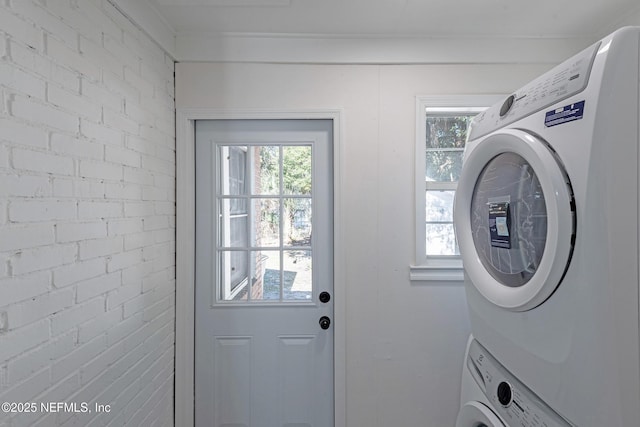 laundry area featuring stacked washer / dryer and brick wall