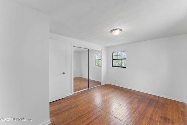 unfurnished bedroom with a textured ceiling, a closet, and hardwood / wood-style floors