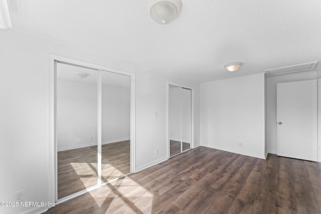 unfurnished bedroom with a textured ceiling, two closets, and dark hardwood / wood-style floors