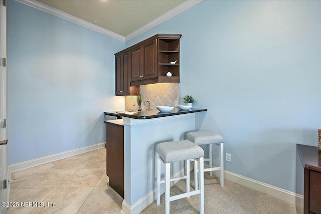 kitchen featuring tasteful backsplash, a breakfast bar area, kitchen peninsula, crown molding, and dark brown cabinets