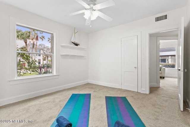 exercise area featuring baseboards, a healthy amount of sunlight, visible vents, and light colored carpet