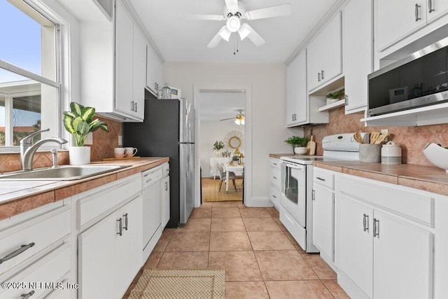 kitchen featuring decorative backsplash, appliances with stainless steel finishes, light tile patterned flooring, a sink, and white cabinetry