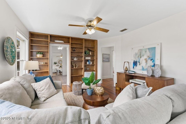 living room with wood finished floors, visible vents, and a ceiling fan