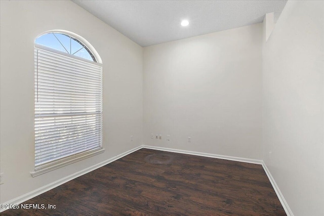 empty room with dark hardwood / wood-style flooring and vaulted ceiling