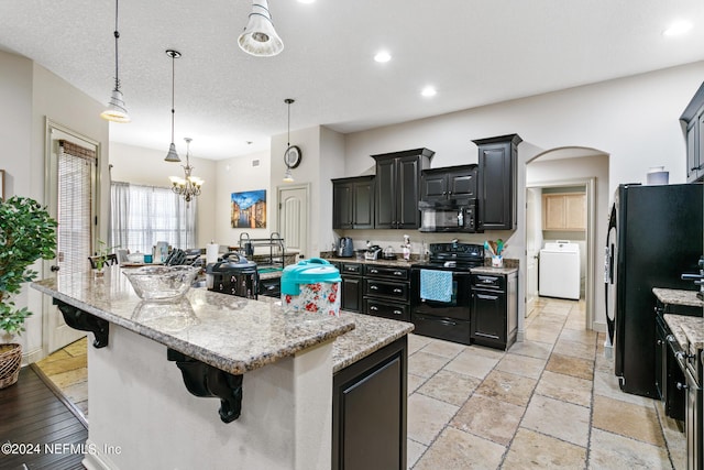 kitchen featuring washer / dryer, a spacious island, black appliances, and pendant lighting