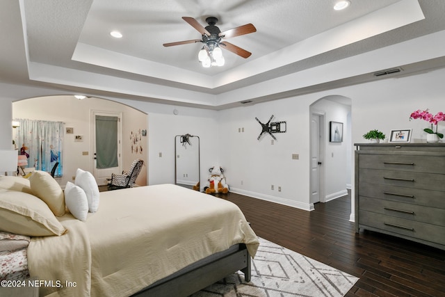 bedroom with a raised ceiling, ceiling fan, and dark hardwood / wood-style floors