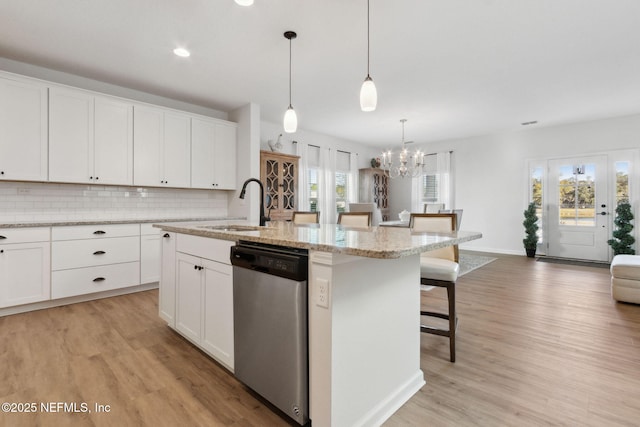 kitchen with decorative light fixtures, dishwasher, a breakfast bar, a kitchen island with sink, and white cabinets