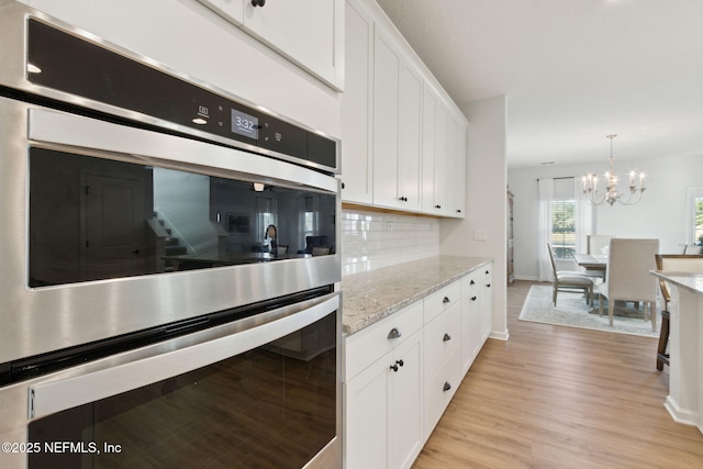 kitchen with decorative backsplash, light stone countertops, white cabinetry, and light hardwood / wood-style floors