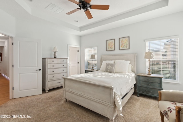 bedroom with ceiling fan, light colored carpet, and a raised ceiling