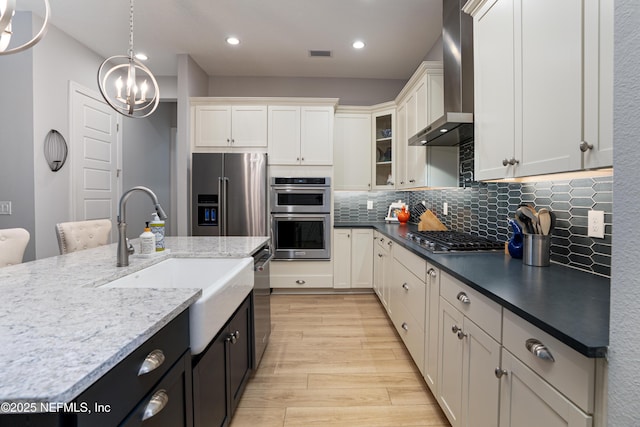 kitchen with stainless steel appliances, white cabinetry, pendant lighting, and wall chimney exhaust hood