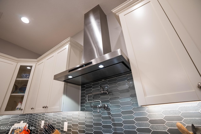 kitchen with wall chimney exhaust hood, vaulted ceiling, and white cabinets