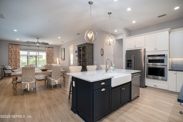 kitchen with white cabinetry, appliances with stainless steel finishes, a kitchen island with sink, and sink