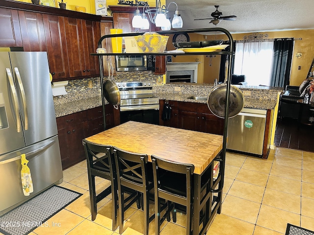 kitchen featuring stainless steel appliances, sink, dark stone countertops, light tile patterned floors, and ceiling fan