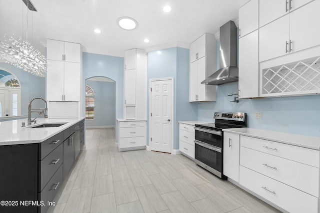 kitchen with decorative light fixtures, wall chimney range hood, range with two ovens, and white cabinetry