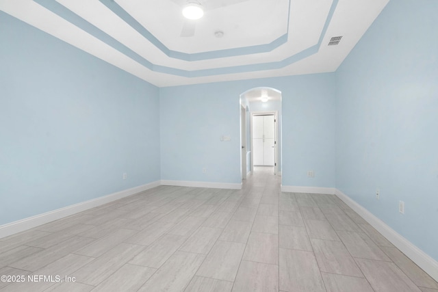 empty room with ceiling fan and a tray ceiling