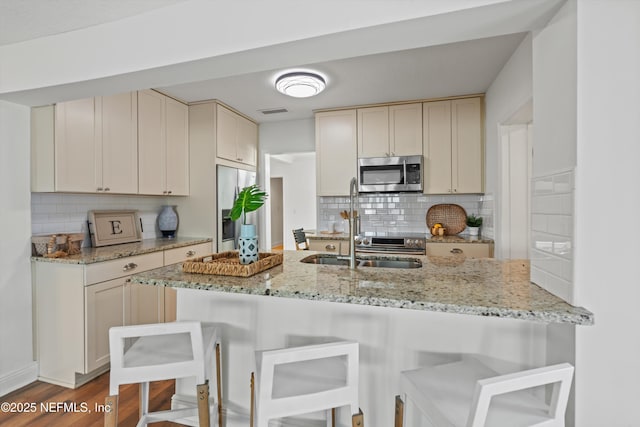 kitchen with appliances with stainless steel finishes, backsplash, light stone countertops, a kitchen bar, and kitchen peninsula