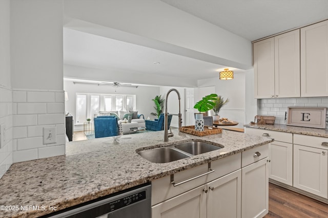 kitchen with sink, white cabinetry, stainless steel dishwasher, light stone countertops, and decorative backsplash