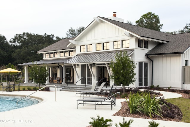 back of house featuring a shingled roof, a patio, a sunroom, a chimney, and board and batten siding