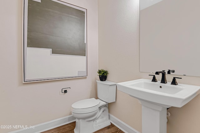 half bathroom with toilet, baseboards, and wood finished floors