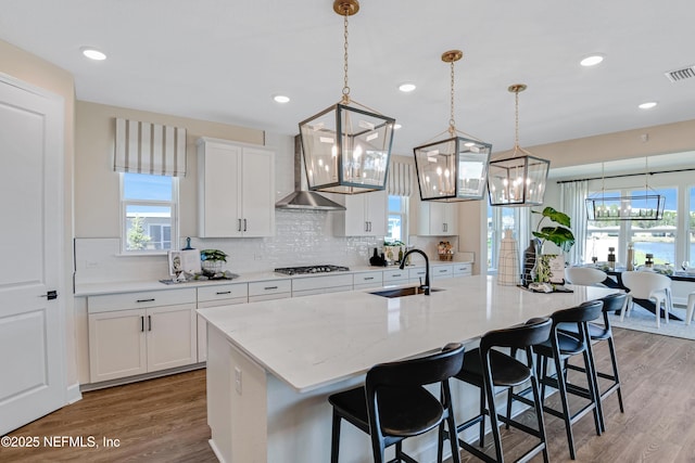 kitchen featuring a kitchen island with sink, a sink, a kitchen breakfast bar, light wood-type flooring, and backsplash