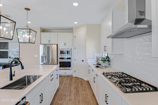 kitchen with a sink, white cabinets, wall chimney range hood, appliances with stainless steel finishes, and light wood-type flooring