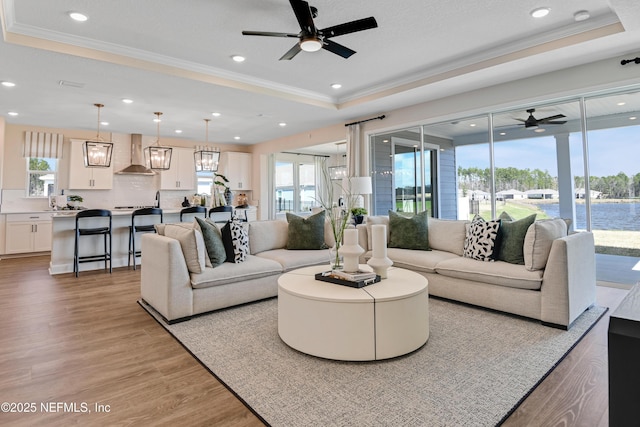 living room featuring light wood-type flooring, a wealth of natural light, a raised ceiling, and ornamental molding