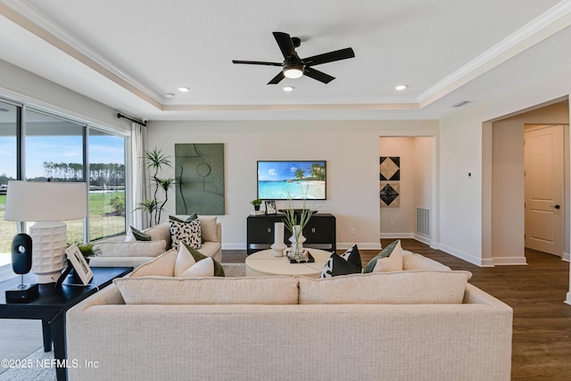 living area featuring a raised ceiling, visible vents, baseboards, and wood finished floors