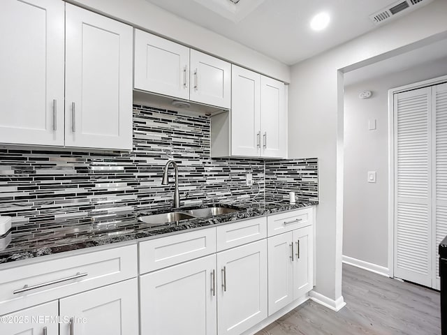 kitchen with white cabinetry, dark stone countertops, light hardwood / wood-style flooring, and sink