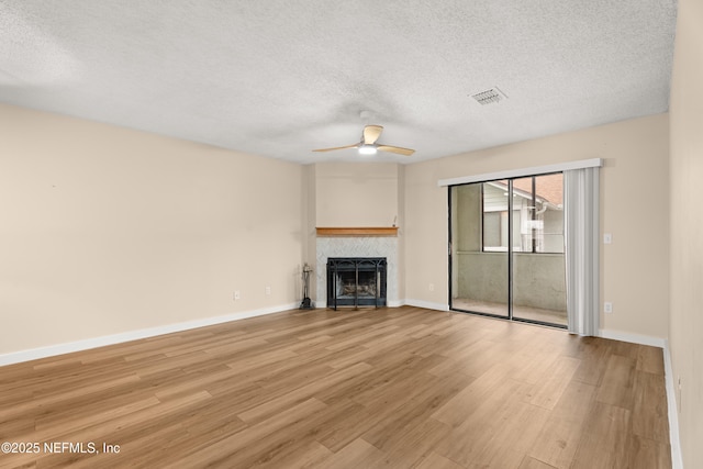 unfurnished living room featuring ceiling fan, a textured ceiling, a tile fireplace, and light wood-type flooring