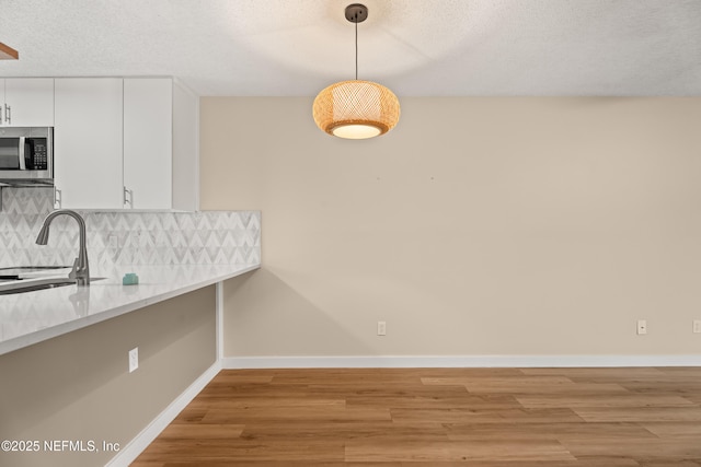 kitchen featuring hanging light fixtures, white cabinets, light wood-type flooring, sink, and backsplash