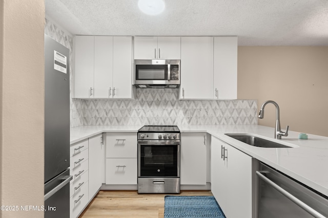 kitchen featuring a textured ceiling, white cabinets, stainless steel appliances, sink, and backsplash