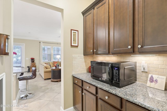 kitchen with light stone counters, backsplash, light tile patterned floors, and crown molding