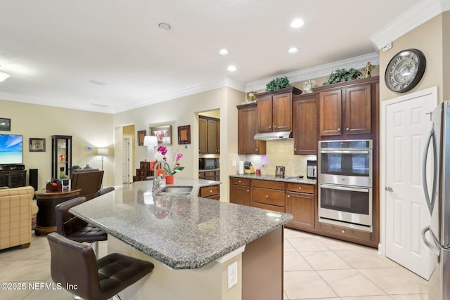 kitchen with appliances with stainless steel finishes, sink, backsplash, a kitchen breakfast bar, and a kitchen island with sink